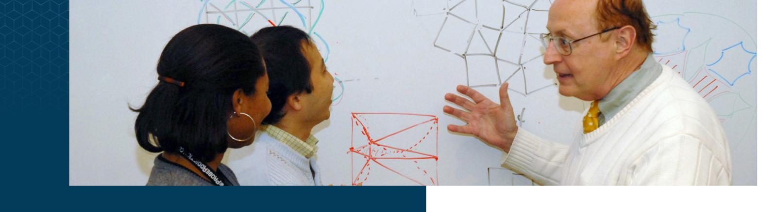 Professor talking two two students in front of a whiteboard